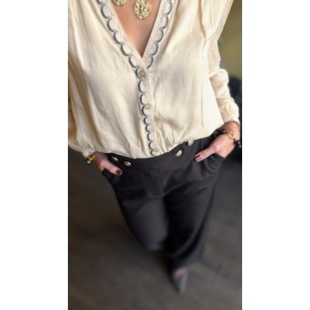 Cette blouse écru et noir allie élégance et confort grâce à sa matière fluide et légère. La broderie fine noire sur la boutonniè
