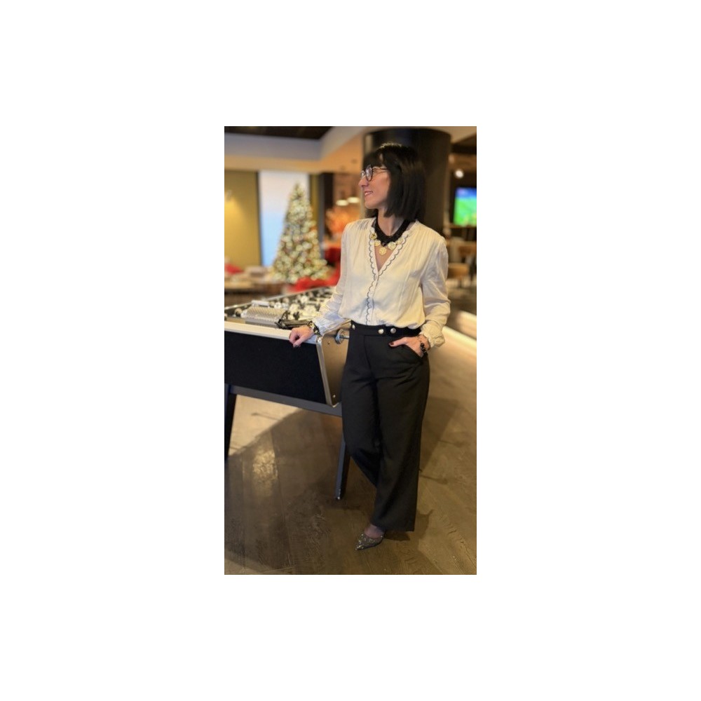 Cette blouse écru et noir allie élégance et confort grâce à sa matière fluide et légère. La broderie fine noire sur la boutonniè